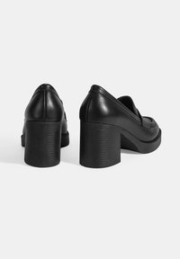 Zwarte leren blockhak schoenen met een ronde neus en een gladde textuur. Kenmerken zijn een gestikte detail op de bovenkant en een stevige hak.
