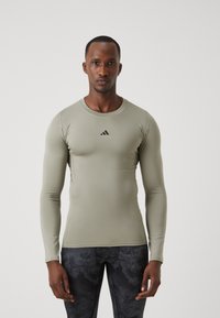 Long-sleeve fitted athletic shirt in light green, made of smooth, stretchy fabric; features black logo on chest and flat seams for comfort.