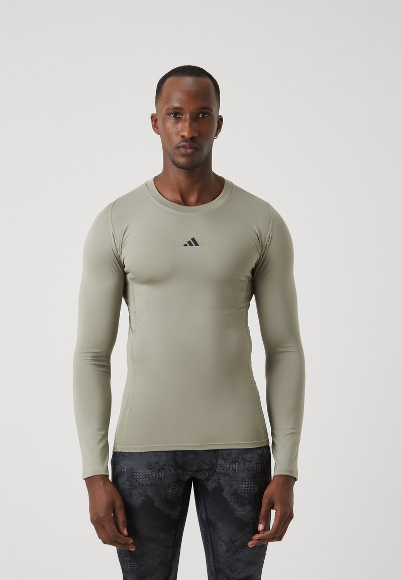 Long-sleeve fitted athletic shirt in light green, made of smooth, stretchy fabric; features black logo on chest and flat seams for comfort.