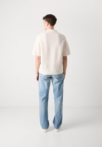 Hvit, teksturert kortermet topp med en avslappet passform, kombinert med lyseblå, løstsittende jeans og hvite joggesko. Enkel design, ingen mønstre.