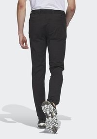 Sorte bukser med lige pasform, sidelommer og baglommer, parret med sorte sportsko med en hvid mønstret sål.