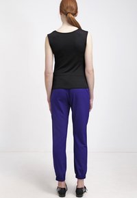 Svart ärmlös topp i kombination med lila byxor med elastiska manschetter. Byxorna har en slät textur, och båda plaggen sitter tight.