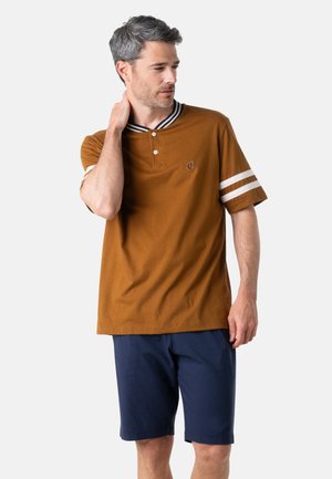 Homme en chemise marron à manches courtes avec des rayures blanches et un short bleu marine, touchant son cou, regardant vers sa gauche sur un fond uni.