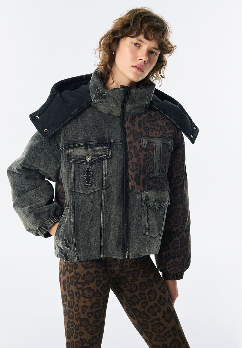 Jeune personne portant une veste à col haut bicolore avec des panneaux en denim usé et imprimé léopard, accompagnée de leggings assortis à imprimé léopard.