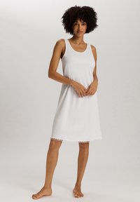 Camisón blanco sin mangas con un corte holgado, que presenta un dobladillo de encaje con forma de concha y una tela suave. El vestido llega hasta la mitad del muslo.