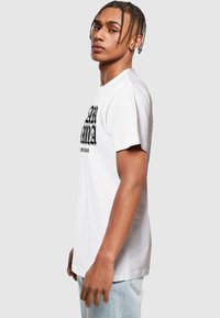 Bílé bavlněné tričko s grafickým potiskem na přední straně, krátkými rukávy a volným střihem, v kombinaci se světle modrými džínovými kalhotami.