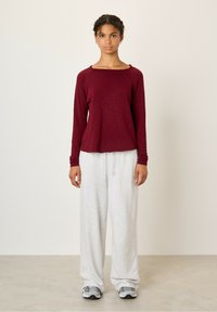 Bordeaux langærmet top med bred udskæring, parret med lysegrå, løstsiddende sweatpants og grå sneakers på en neutral baggrund.