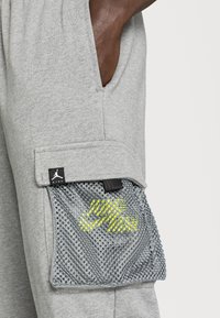 Graue Sportshorts mit einer Netztasche mit gelbem Muster, elastischem Bund und einem sichtbaren Logoetikett an der Seite.