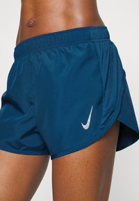 Mörkblå sportshorts gjorda av lättviktsmaterial, med en silverlogotyp, elastisk midja och nätpaneler på sidorna för andningsförmåga.