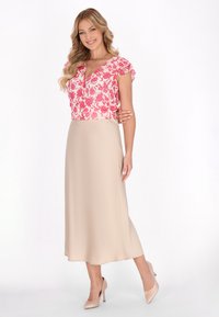 Blomstret lyserød bluse med flagrende ærmer, parret med en beige midi-nederdel. Glat tekstur og tætsiddende design suppleret med nude højhælede sko.