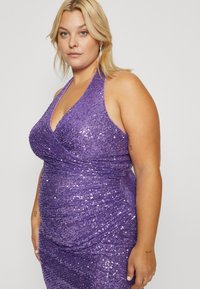 Robe en sequins violette avec un col halter et un design enveloppant, présentant une silhouette ajustée et une surface texturée. Accentuée par des sequins scintillants.