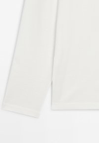 White long sleeve shirt sleeve and hem on a light background, showing fabric texture and stitching details.