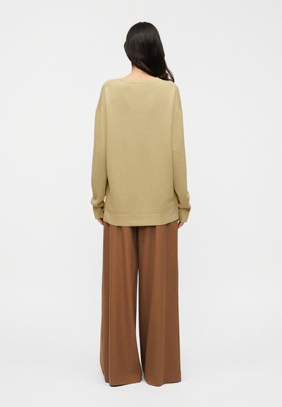 Pull beige oversize en tissu texturé, manches larges et encolure arrondie, associé à un pantalon marron à jambes larges.