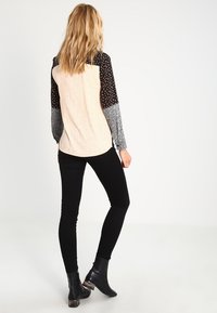 Långärmad topp med beige strukturerad kropp och svarta mönstrade ärmar. Parat med svarta tajta byxor och ankelstövlar, sedd från baksidan.