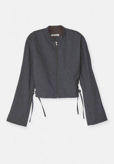 Hall kaelusega lühike särgid, esi tõmblukuga ja pikad kellukesed. Omab külgtukke ja sileda tekstuuriga kangast.