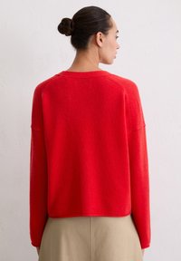 Czerwony, przytulny sweter o luźnym kroju, z okrągłym dekoltem i długimi rękawami. Widok od tyłu, ukazujący fakturowaną tkaninę i detale na krawędzi.