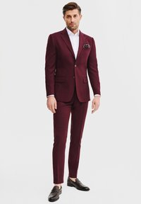 Burgundzkie garnitur o dopasowanym kroju, z klapami w szpic, dwoma guzikami i chusteczką w kieszeni. W zestawieniu z białą koszulą i ciemnymi mokasynami.