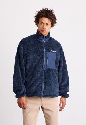 Tengerészeti polár dzseki magas gallérral, cipzárral és elülső mellzsebbel. Puha tapintású, rugalmas mandzsettákkal rendelkezik. Logó a mellkason.