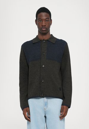 Button-up jacket in textured dark green and navy, featuring a collared neckline, long sleeves, and contrasting color blocks on the shoulders.