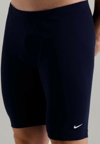 Shorts de bain navy en tissu extensible, avec une coupe ajustée, une texture lisse et un petit logo Nike blanc en bas à gauche.