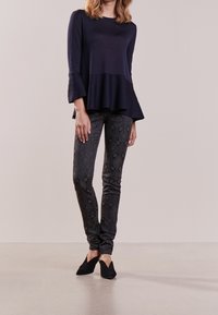 Navy långärmad topp med utsvängda ärmar, i kombination med figursydda svarta byxor med en texturerad paisleymönster och svarta slipskor.