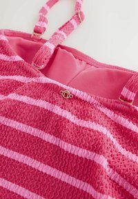 Lyserød stribet top med tekstureret stof med smock-detalje. Justerbare stropper og en lille gulddetalje foran. Foret inderside.