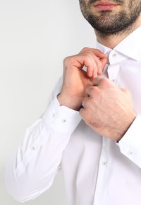 Biała koszula wizytowa z kołnierzykiem zapinanym na guziki, niebieskie kwiatowe akcenty na mankietach oraz niebieskie guziki. Tkanina wygląda na gładką i dobrze dopasowaną.