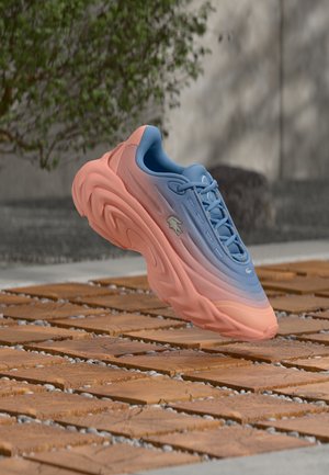 Baskets Lacoste avec une tige dégradé bleu clair et corail, matériau texturé, semelle surélevée, et logo emblématique sur le côté.