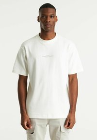 T-shirt bianco in cotone con maniche corte, scollatura rotonda e un logo stampato sul petto. Texture liscia e morbida.