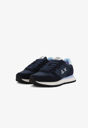 Un paio di sneaker blu navy con suole bianche, lacci neri e testo "LE RAGAZZE CORRONO VELOCE" sulla linguetta, angolato su uno sfondo bianco.