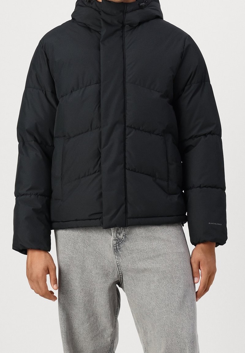 Black puffer jacket with a hood, featuring quilted sections, side pockets, and elastic cuffs. Made from a smooth, matte fabric.