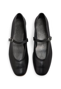 Schwarze Leder-Mary-Jane-Schuhe im Stil mit abgerundetem Zehenbereich, flacher Sohle und verstellbarem Riemen mit einer kleinen silbernen Schnalle. Glatte Textur.