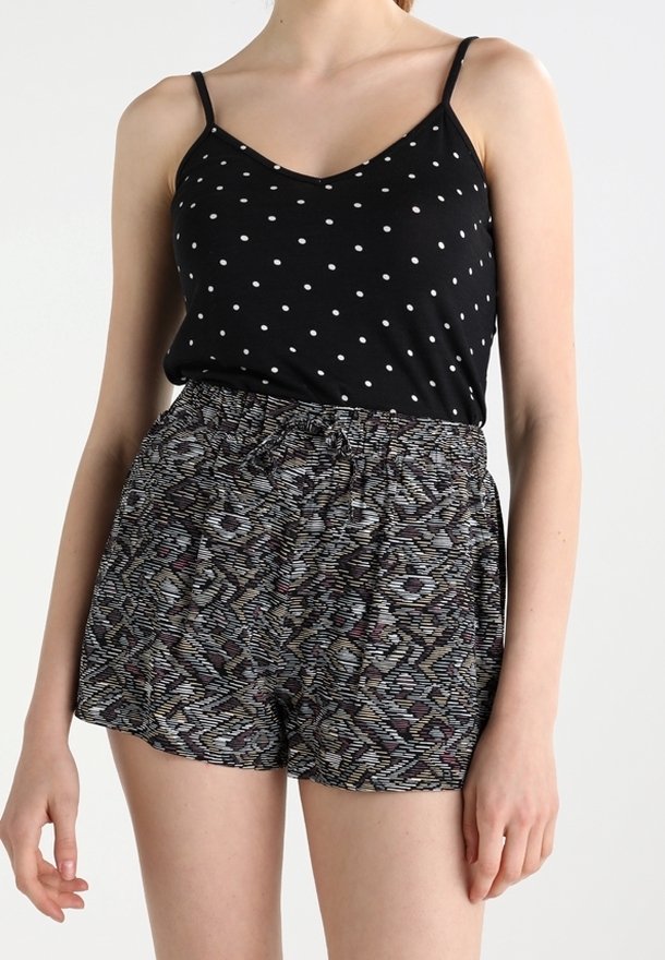 Débardeur noir à pois avec des fines bretelles, associé à un short ample à motifs dans des nuances de gris, violet et bleu. Détail de taille élastique.