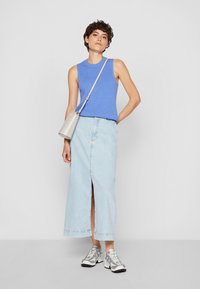 Jasnoniebieski prążkowany top bez rękawów, o wysokim dekolcie, w zestawieniu z jasnoniebieską długą spódnicą dżinsową z przednim rozcięciem oraz srebrnymi butami sportowymi.