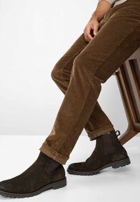 Pantaloni in corduroy marrone con texture a righe, abbinati a stivali alla caviglia in suede marrone scuro con inserti in rete e suole in gomma.