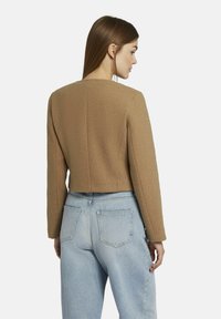 Korte, bruine wolmix jack met een rechte achterkant en lange mouwen; gecombineerd met lichtblauwe high-waisted jeans.