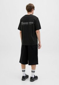 Sort bomuld T-shirt med korte ærmer og ryggrafik. Sammen med sorte shorts, hvide sokker med sorte striber og sorte sneakers.
