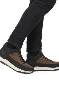 Zapatillas altas en marrón y negro con un upper texturizado, diseño de cordones y detalles de suela de goma robusta. Combinadas con vaqueros negros.