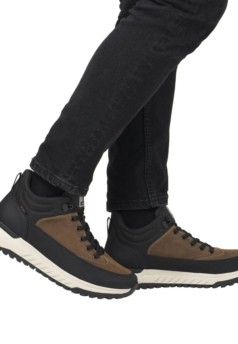 Zapatillas altas en marrón y negro con un upper texturizado, diseño de cordones y detalles de suela de goma robusta. Combinadas con vaqueros negros.