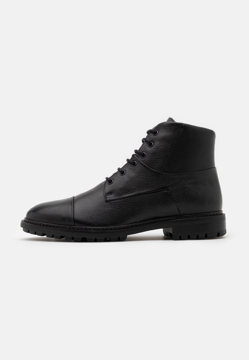 Bottine en cuir noir avec surface texturée, laçage sur le devant, bout lisse et semelle épaisse et robuste sur un fond clair uni.