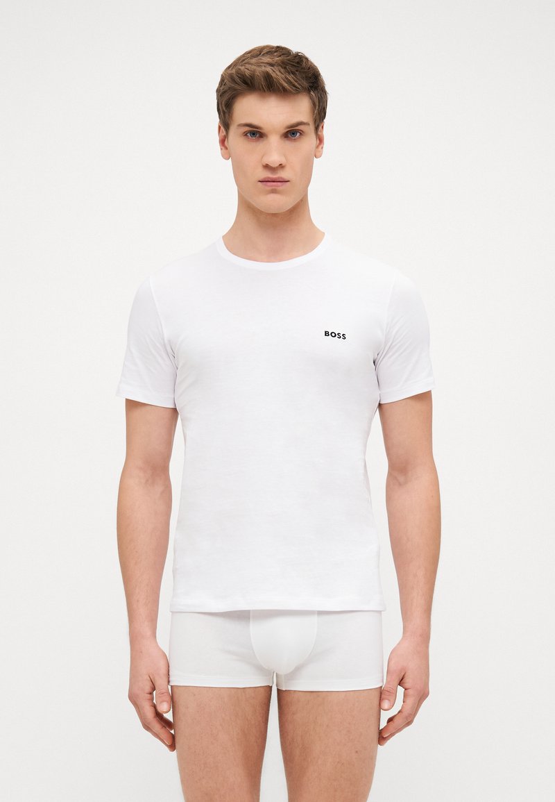 T-shirt blanc à manches courtes en coton avec un col rond et un petit logo "BOSS" noir sur la poitrine gauche, associé à un sous-vêtement blanc.