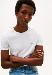 Wit katoenen t-shirt met een ronde hals en korte mouwen, met een klein geborduurd logo in rood, wit en blauw op de borst.