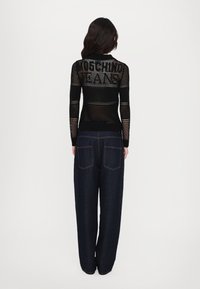 Black mesh long-sleeve top with "Moschino Jeans" text on the back, paired with loose-fitting dark denim pants featuring rear pockets.