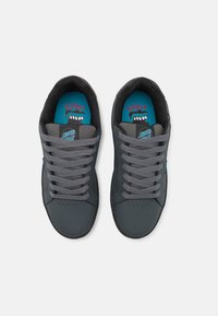 Adidași gri cu o finisare netedă, sintetică, având șireturi gri, o talpă neagră și branțuri albastre cu un design grafic.