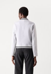Gray sweatshirt with a ribbed, striped collar and waistband, featuring long sleeves and a structured design. Back view shows minimal seams.