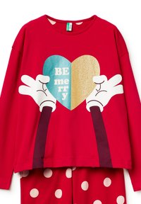 Červený top s dlouhým rukávem se srdíčkovou grafikou, na které je nápis "BE merry" modrou a zlatou třpytivou barvou, bílé motivy rukou, doplněný o pyžamové kalhoty s puntíky.
