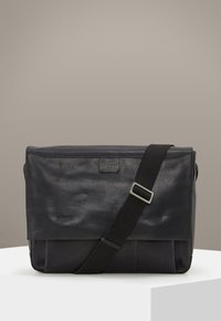 Borsa a tracolla in pelle nera con finitura testurizzata, tracolla regolabile, chiusura a pattina e un'etichetta del marchio sulla parte anteriore.