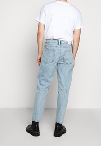 Jeans de denim azul claro con un corte relajado, que cuentan con una cinturilla elástica, cinco bolsillos y un diseño de pierna ligeramente ajustada.