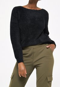 Černý, texturovaný svetr s uvolněným střihem a širokým výstřihem, kombinovaný s olivově zelenými cargo kalhotami s kapsami.