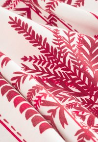 Stof met een rood varenpatroon op een witte achtergrond, met een zachte textuur en vloeiende, gladde plooien.